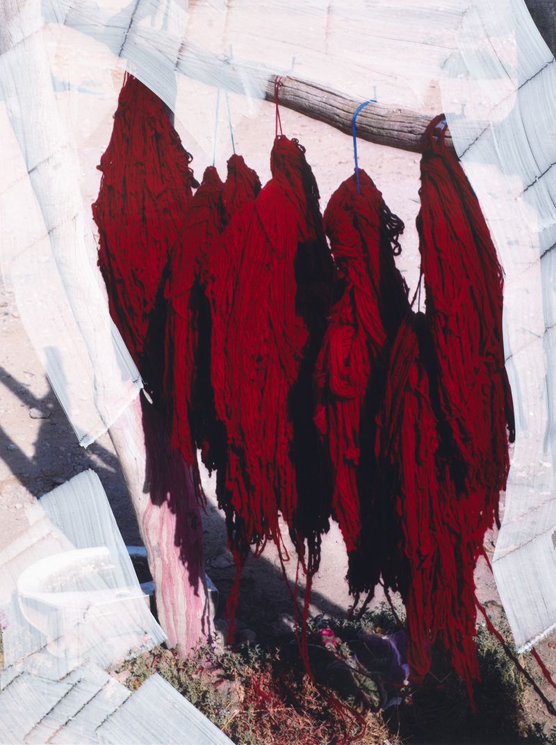 Group of vibrant red skeins of wool yarn hanging on a wooden frame, bathed in natural light with filtered shadows. Rustic and raw.