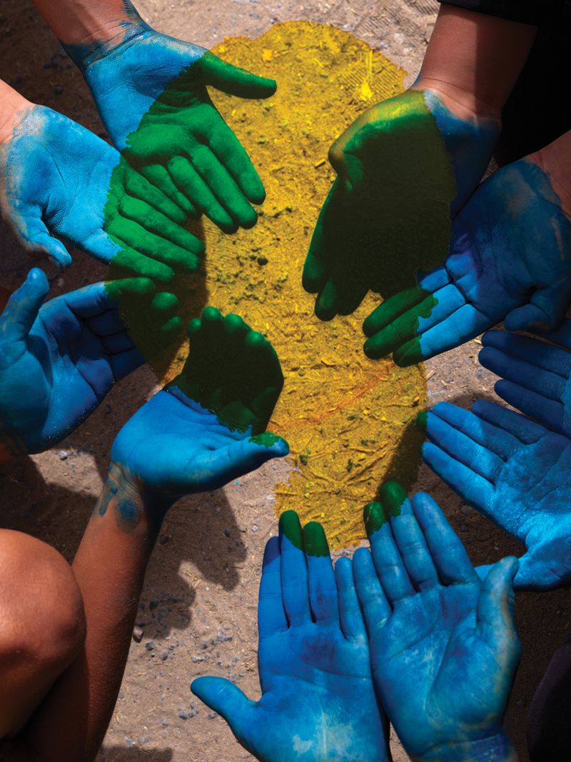Close-up overhead shot of a group of diverse hands painted with green and blue paint surrounding a yellow-painted circular surface.