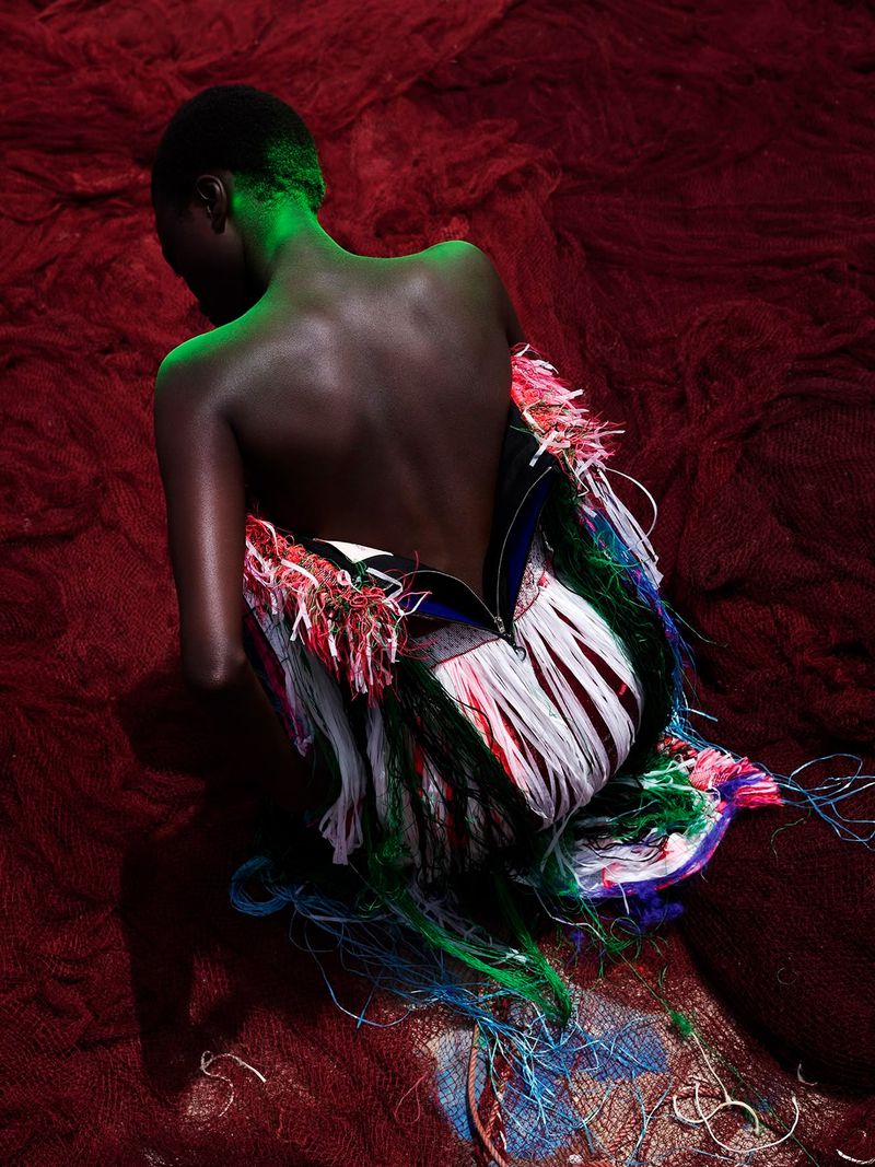 Back view of dark-skinned woman in fringed dress, spotlight on hair, red textured background. Fashion, beauty, and creative photography.