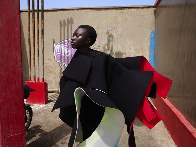 Striking image of a Black woman posing in an avant-garde fashion outfit against an urban backdrop with graffiti, showcasing bold design and style.