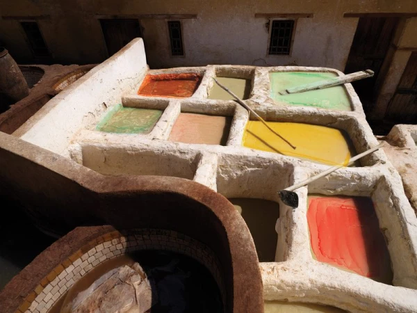 Aerial view of the Chouara tanneries in Fez, Morocco, featuring vats of colorful dyes, stone architecture, and wooden tools.