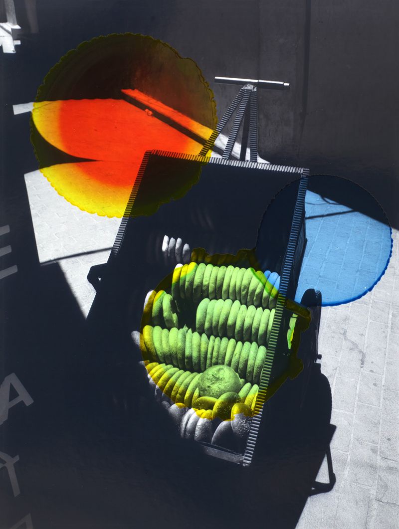 Abstract art featuring a stack of organic materials in a black container against a dark wall, with colorful light filters.