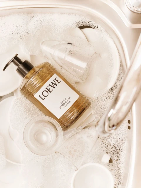 Loewe liquid soap bottle and clear glasses in a sink full of soapy water, highlighting cleanliness and a spa-like home environment.