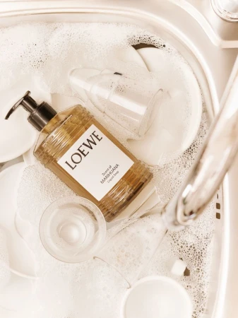 Loewe liquid soap bottle and clear glasses in a sink full of soapy water, highlighting cleanliness and a spa-like home environment.