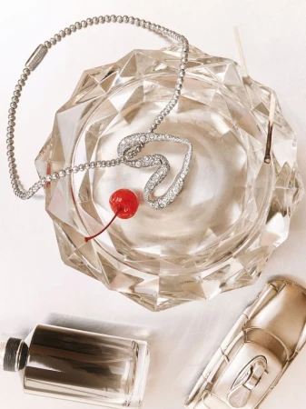 Close-up still life of a crystal ashtray holding a heart-shaped diamond necklace with a cherry, plus perfume and car model.