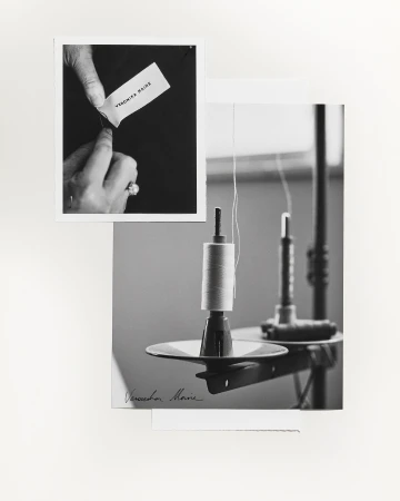 Black and white photograph featuring a spool of thread and a hand holding a tag in a minimalist studio setting, classic and refined.