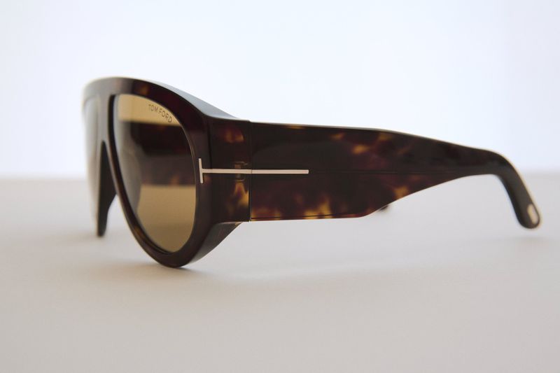 Tortoiseshell Tom Ford sunglasses with gold lenses and T logo on a white surface, showcasing side profile and design details.