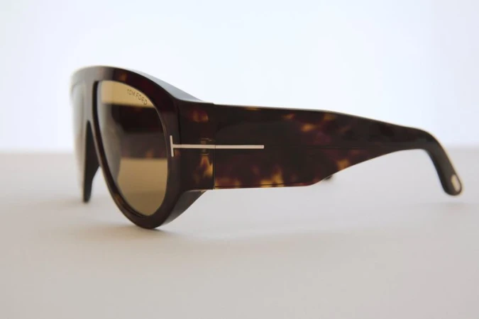 Tortoiseshell Tom Ford sunglasses with gold lenses and T logo on a white surface, showcasing side profile and design details.