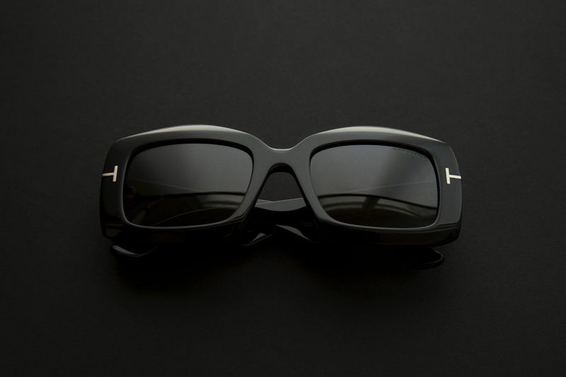 Black-rimmed sunglasses with dark lenses are centered on a dark background, showcasing their modern design and sleek aesthetic.