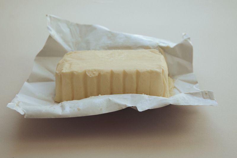 Close-up of butter in foil wrapping, studio shot. Perfect for food photography, dairy product advertising, or culinary-themed content.