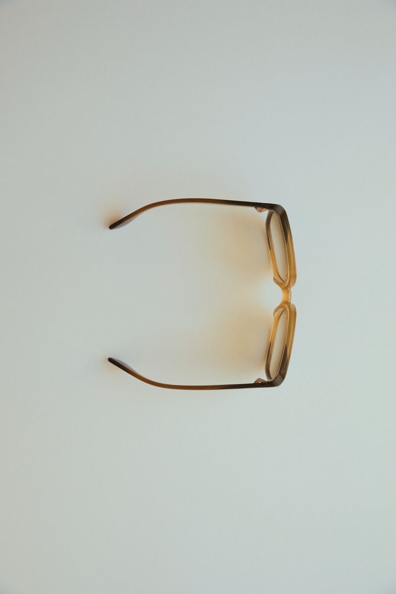 Overhead shot of tan-framed glasses on a white background with warm lighting and shadows, creating a clean and minimalist aesthetic.