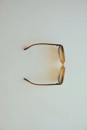 Overhead shot of tan-framed glasses on a white background with warm lighting and shadows, creating a clean and minimalist aesthetic.
