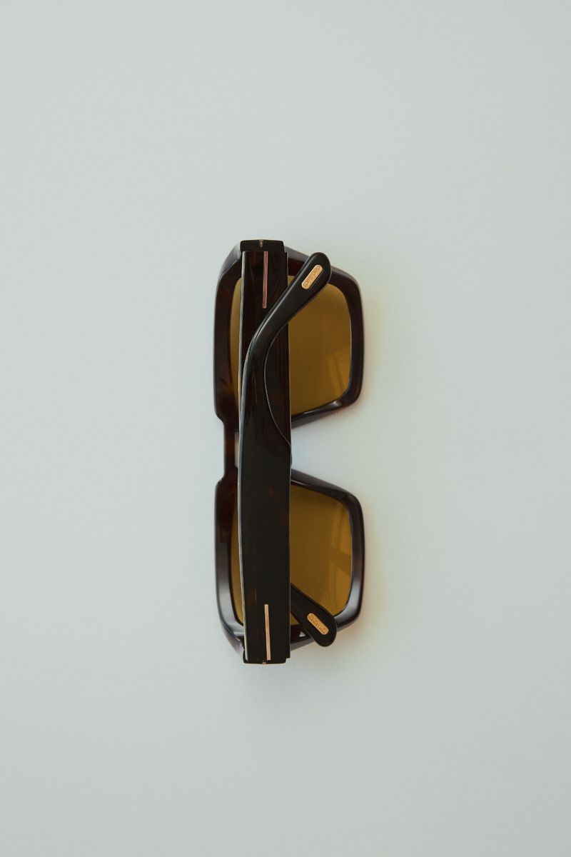 Elevated view of dark, folded sunglasses with gold accents on a white surface, product shot for eyewear fashion and accessories.