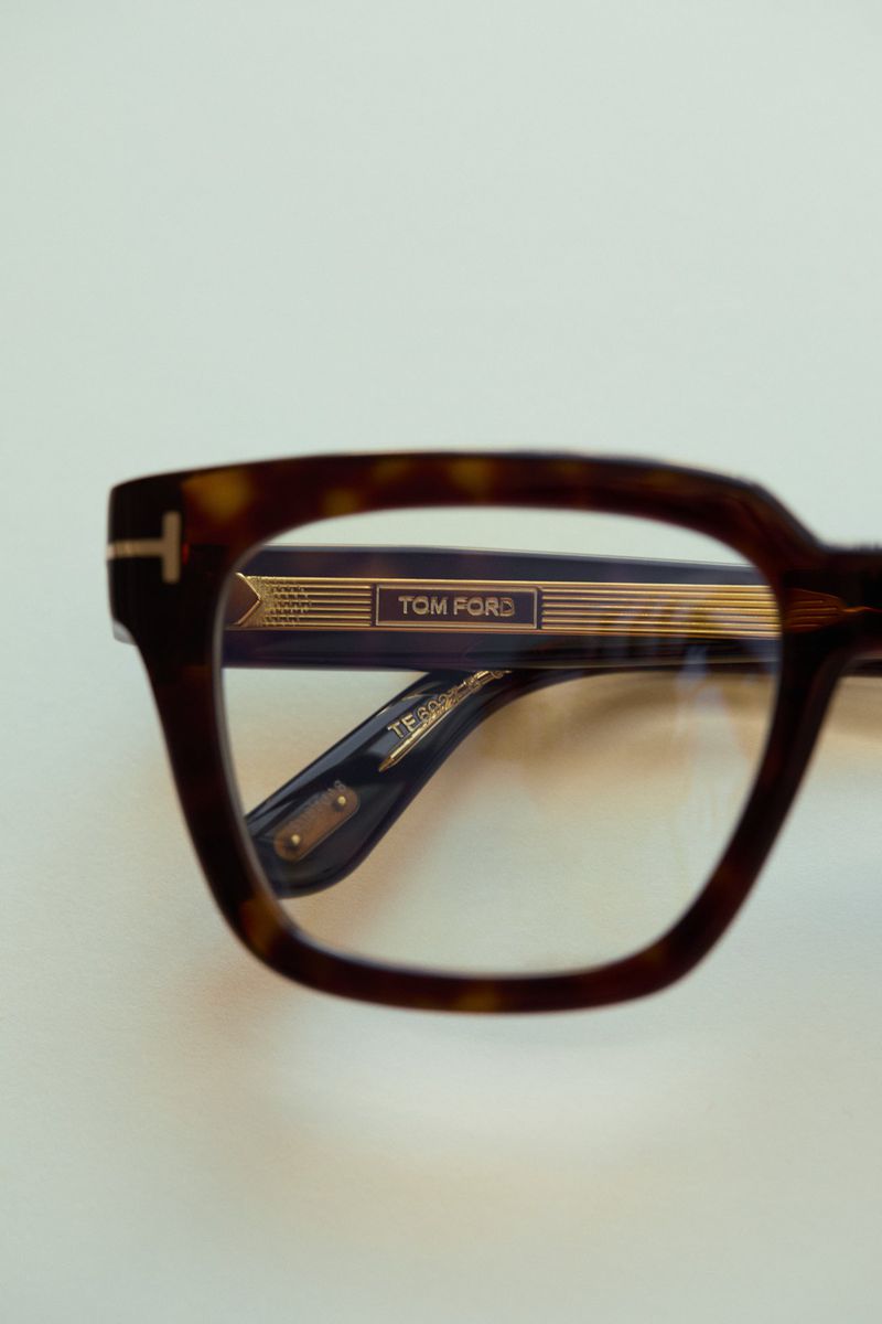 Close-up of tortoiseshell Tom Ford eyeglasses on a white surface, highlighting the frame's pattern, gold accents, and lens shape.