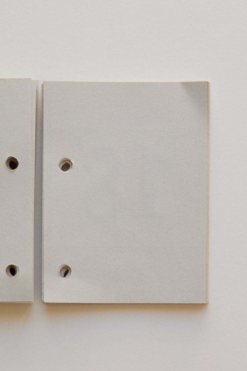 Two light gray rectangular boards with rounded corners and holes, arranged on a light gray background, creating a minimalist composition.