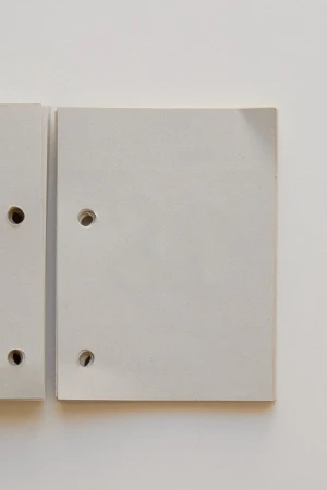 Two light gray rectangular boards with rounded corners and holes, arranged on a light gray background, creating a minimalist composition.
