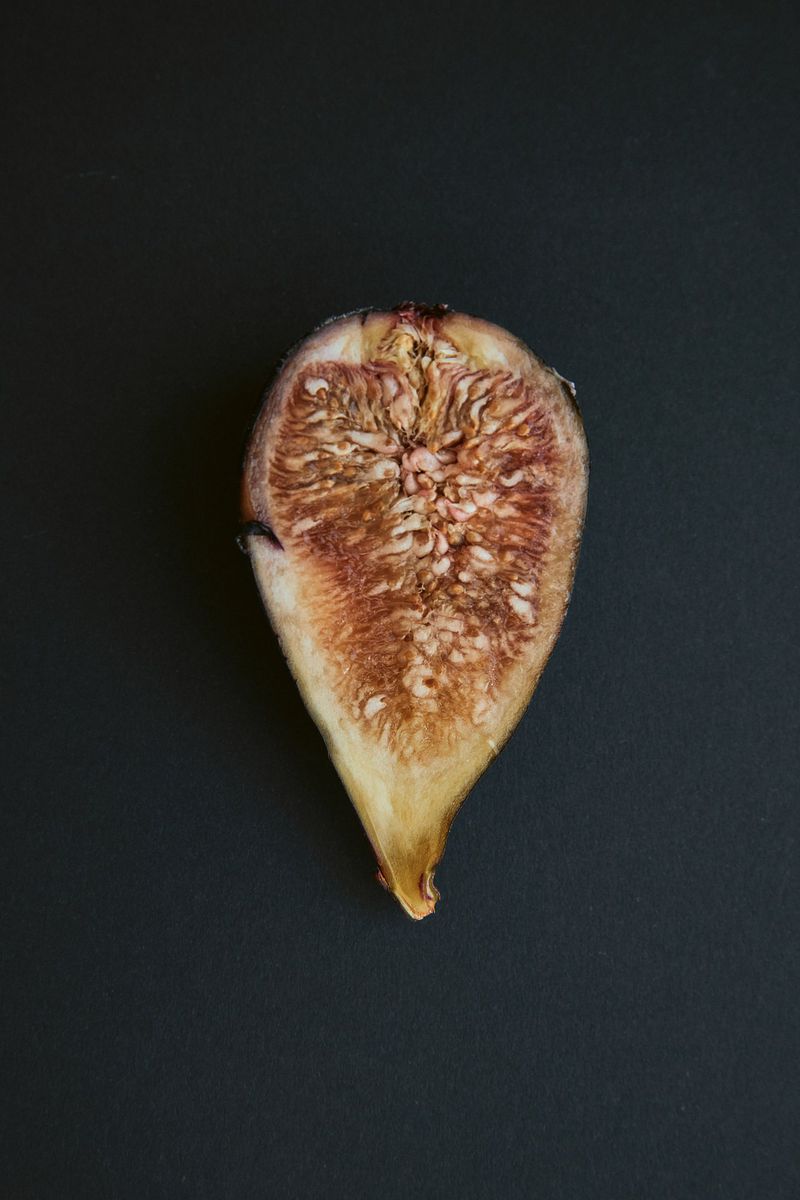 Studio shot of a halved, dried fig against a dark background. The fig's interior is visible, showcasing seeds and pulp.