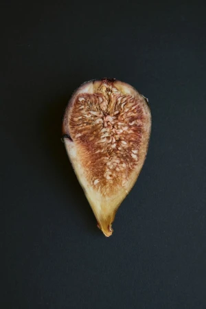 Studio shot of a halved, dried fig against a dark background. The fig's interior is visible, showcasing seeds and pulp.