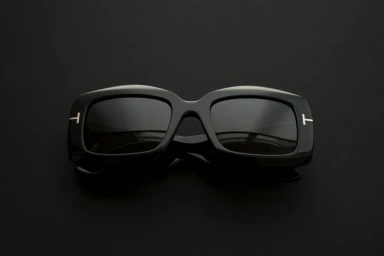 Black rectangular acetate sunglasses with silver T temple accents positioned centered on a dark seamless background.