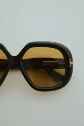 Close-up of black designer sunglasses with amber tinted lenses and gold metal accents on a pale background.