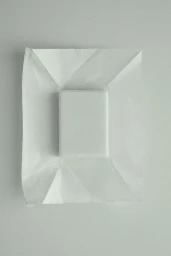 A white rectangular bar resting on top of unfolded, creased white wrapping paper against a neutral studio backdrop.