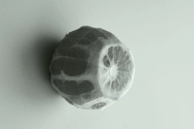 Monochrome close-up of a geometrically carved and peeled citrus fruit on a light neutral surface.