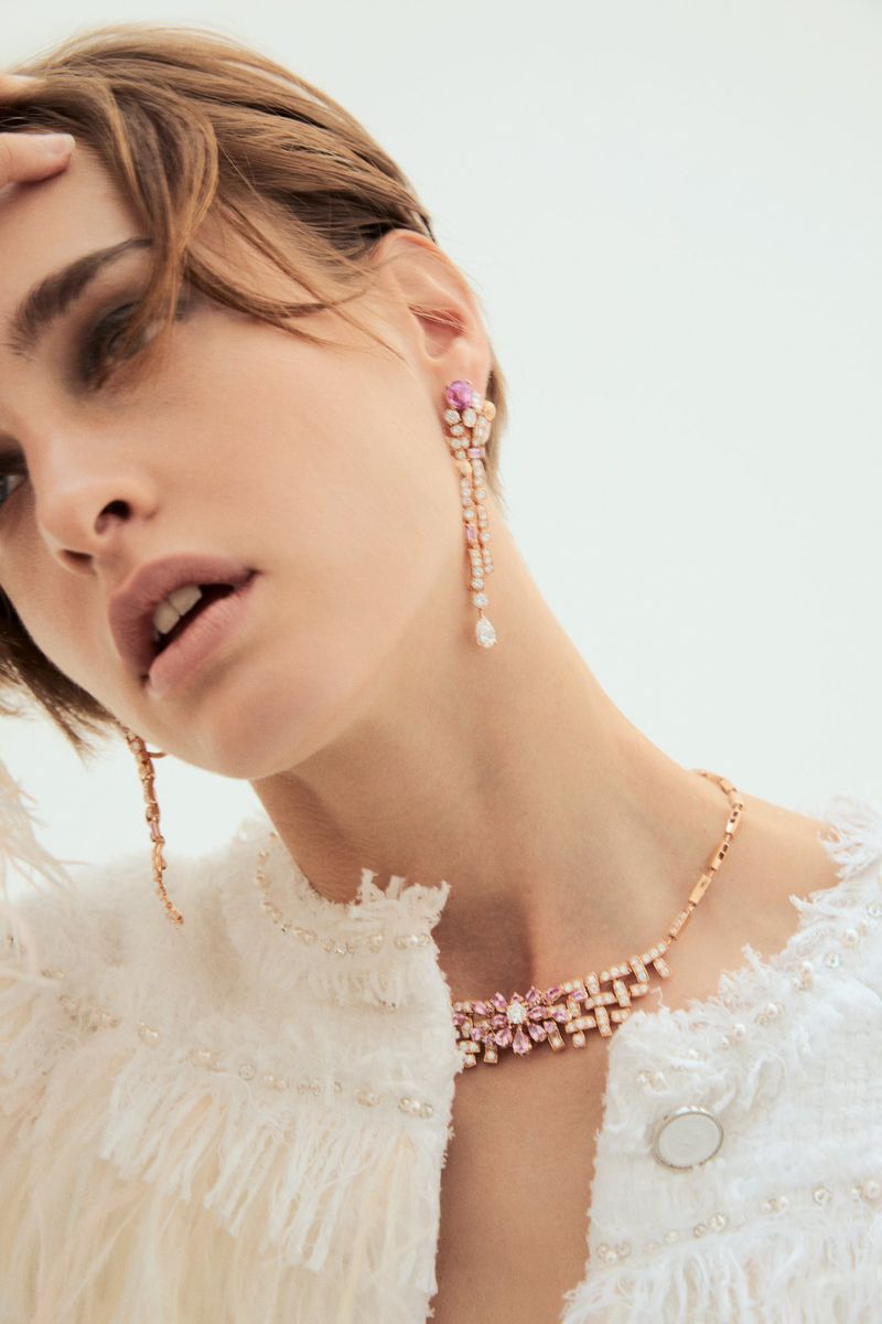 Close-up of a woman wearing a white textured jacket and pink floral jewelry set consisting of a necklace and dangling earrings.