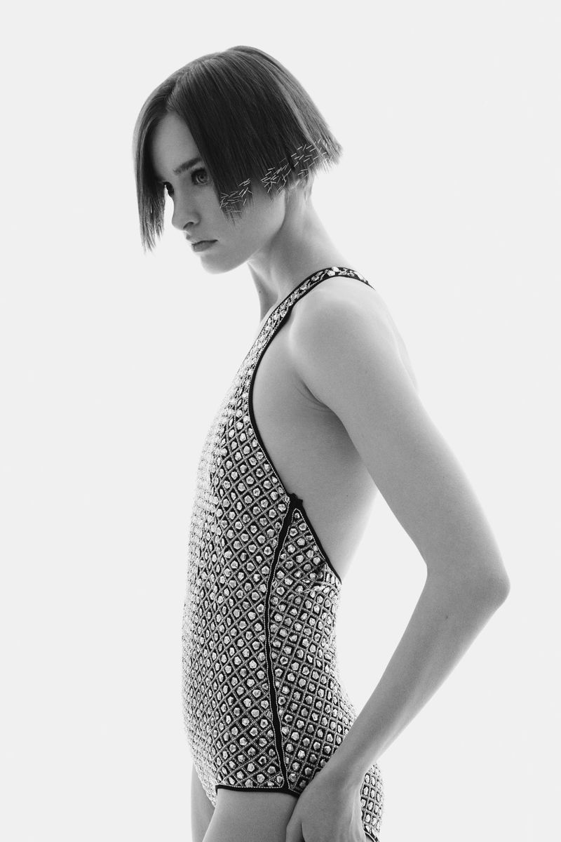 Monochrome portrait of a female model in a patterned bodysuit with geometric bob and side profile against a clean white backdrop.