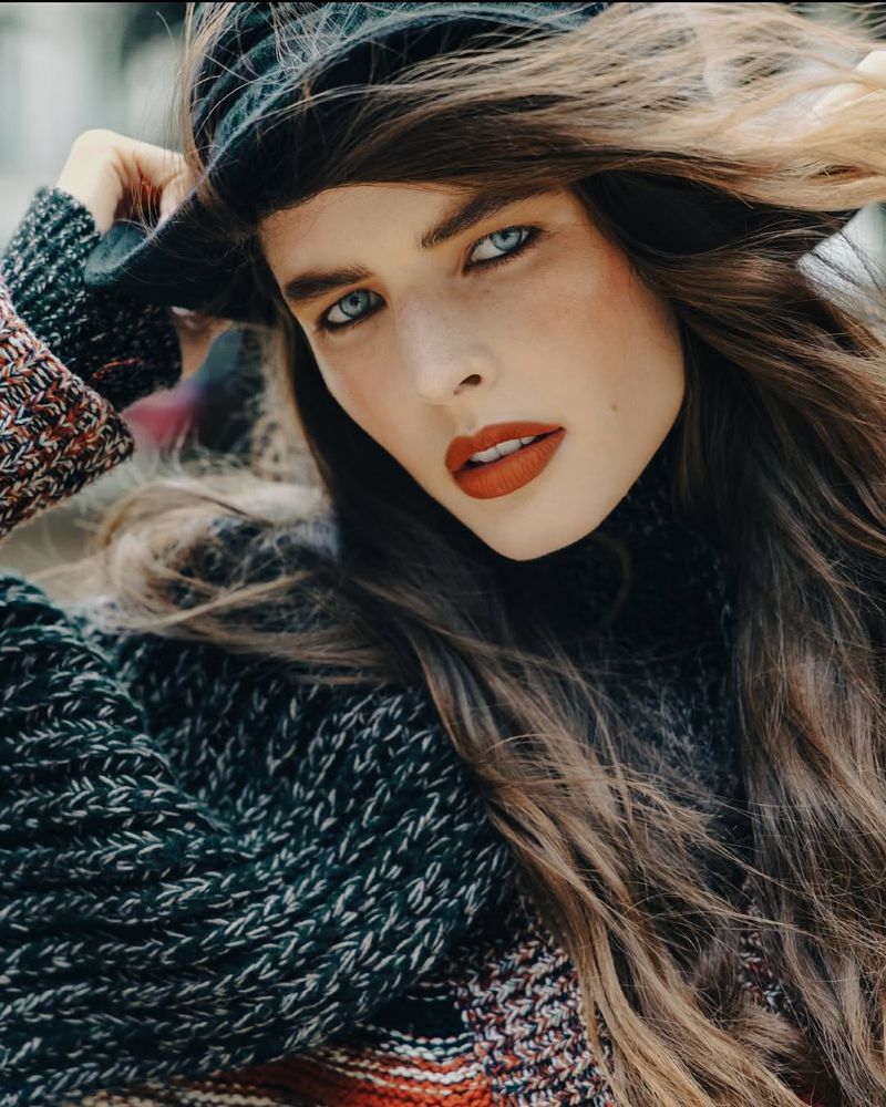 Close-up portrait of model Libby Taverner with windswept hair wearing a chunky knit sweater and black hat.