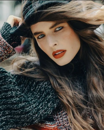Close-up portrait of model Libby Taverner with windswept hair wearing a chunky knit sweater and black hat.