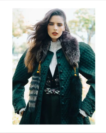 Brunette woman in quilted coat with fur collar and trim poses outdoors in a fashion shot with diffused natural lighting.