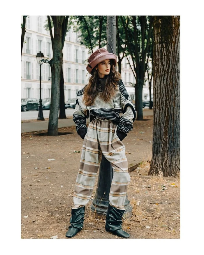 Model Libby Taverner wearing a pink hat, knit sweater, and wide plaid trousers outdoors in Paris for D Repubblica.
