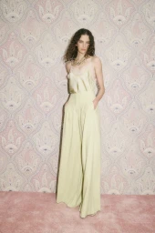 Model Africa Garcia in a pale yellow silk camisole and wide-leg trousers posing in front of pink paisley patterned wallpaper.