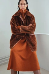 Model in a brown faux fur coat and rust-colored dress against a plain white studio background