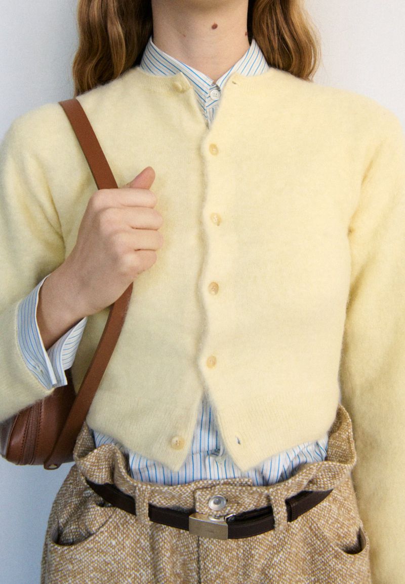 Fashionable outfit featuring a woman wearing a yellow cardigan, striped shirt, and patterned pants, accessorized with a brown shoulder bag.