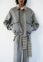 Model wearing a grey wool bomber jacket and matching trousers against a plain white background for Auralee fall/winter 2025 lookbook.