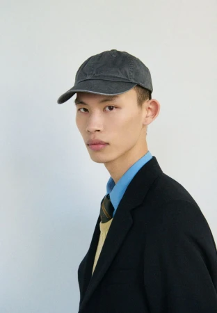 Model Yura Nakano wearing a dark grey baseball cap, black blazer, and light blue collared shirt against a plain background.