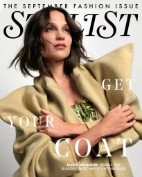 Alicia Vikander wearing a structured tan coat with folded arms against a white background for Stylist Magazine UK.
