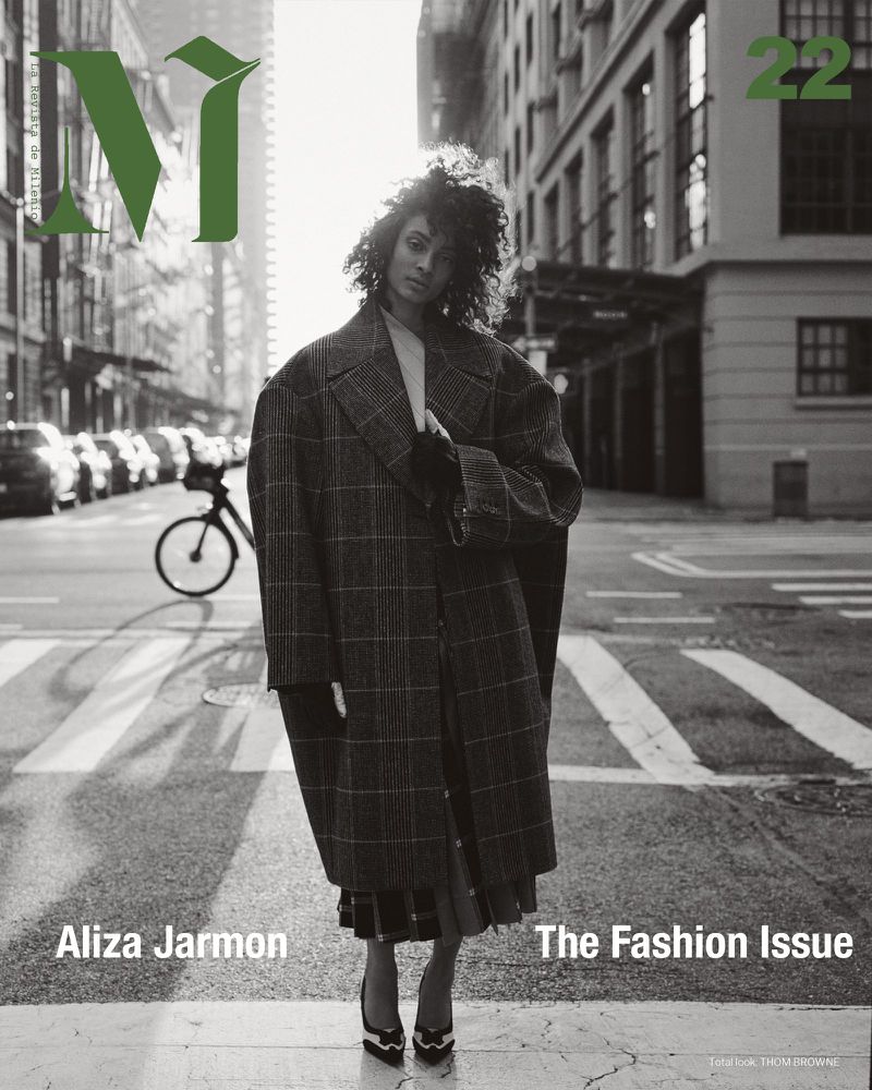 Magazine cover featuring a woman in a plaid coat standing on a city street with buildings and a bicycle in the background.
