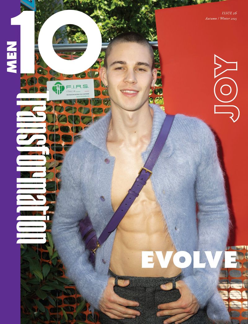 Magazine cover featuring a smiling man in a cardigan with a purple shoulder bag standing outdoors in front of a red wall and foliage.