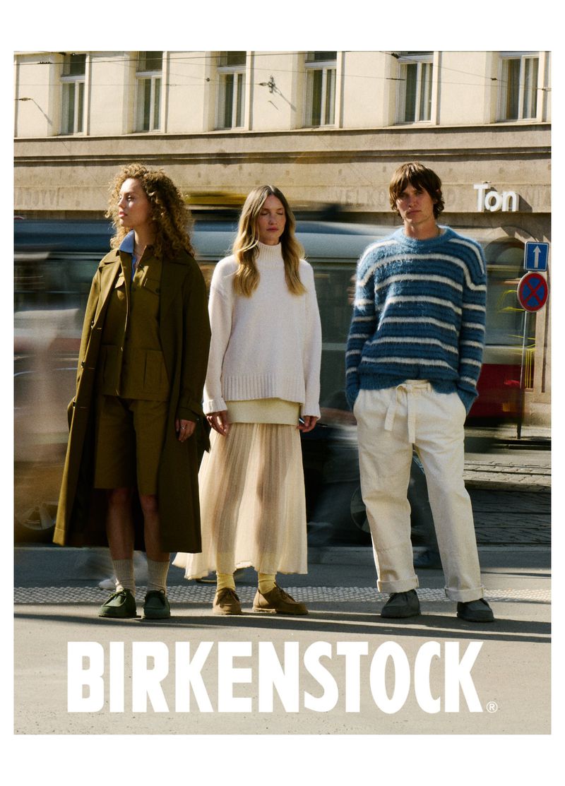 Three models in outdoor fashion shot, wearing Birkenstock shoes. Two women and one man are standing on a city street in daytime.