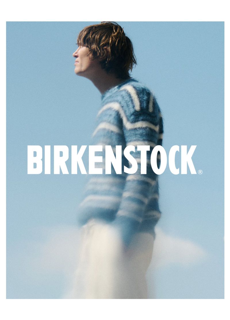 Fashion shot features a person in a patterned blue and white sweater against a blue sky, wearing Birkenstock. Apparel advertisement.