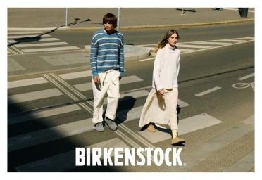 Two models walking across a city street crosswalk for a Birkenstock campaign, wearing casual knitwear and footwear.