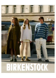 Three models standing in street fashion outfits wearing Birkenstock shoes with motion-blurred city traffic behind them.