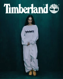 Kiko Mizuhara in a white sweatshirt and trousers against a dark green textured background for Timberland Advice of an Icon Fall 2025.