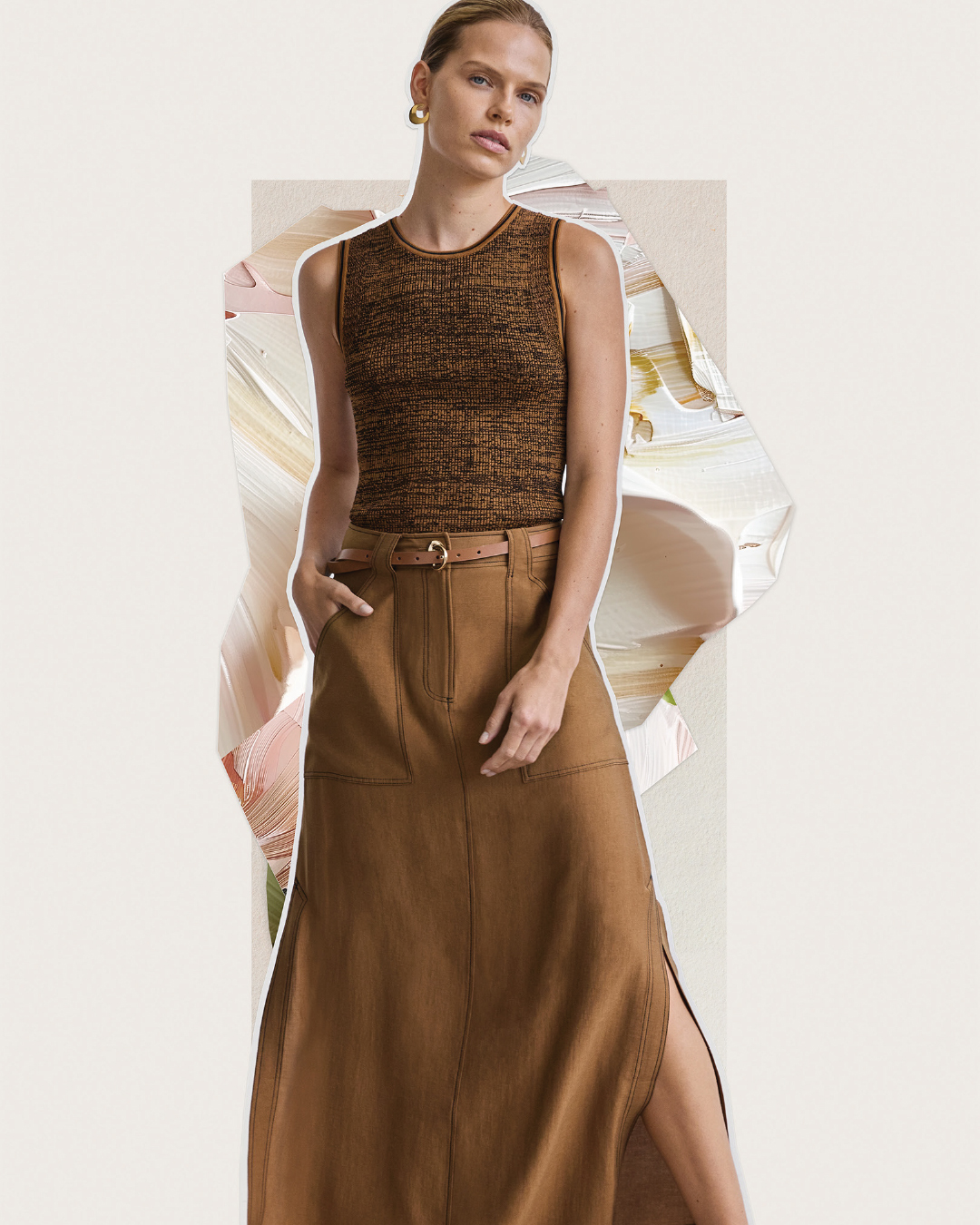 Adult female fashion model poses in a sleeveless brown top and long brown skirt with a graphic white background with paint effects.
