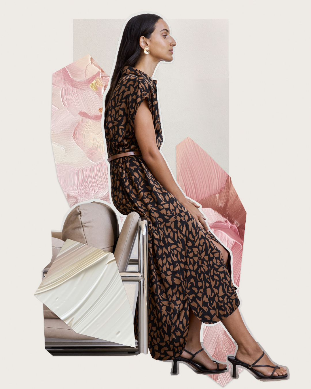 A woman models a black and brown leaf-print midi dress with a belt and black heeled sandals, sitting on a silver chair. 