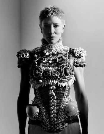 Monochrome portrait of adult woman in a highly textured, custom-made dress with distinctive embellishments and short hair, set against a plain background.