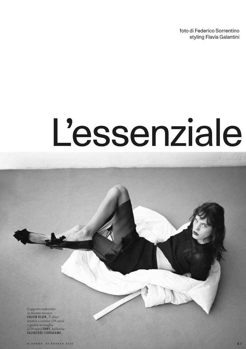 Editorial fashion shot of a woman lying on a white pillow wearing black separates with dramatic eye makeup in a photo studio.