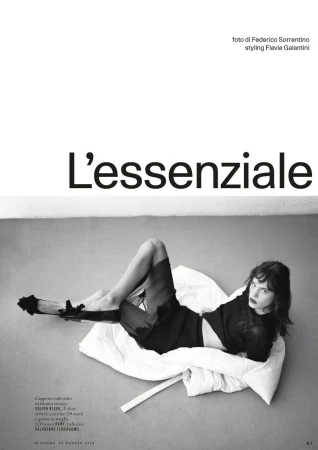 Editorial fashion shot of a woman lying on a white pillow wearing black separates with dramatic eye makeup in a photo studio.